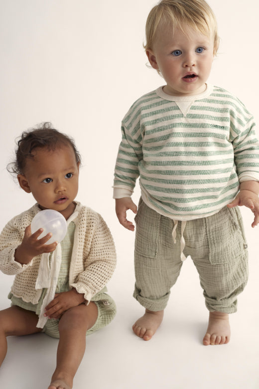 Zwei Kinder. Junge trägt ein Unisex Baby Sweatshirt mit grünen Streifen aus nachhaltiger Bio-Baumwolle. Perfekt für Jungen und Mädchen, ideal für Alltag und Spiel.