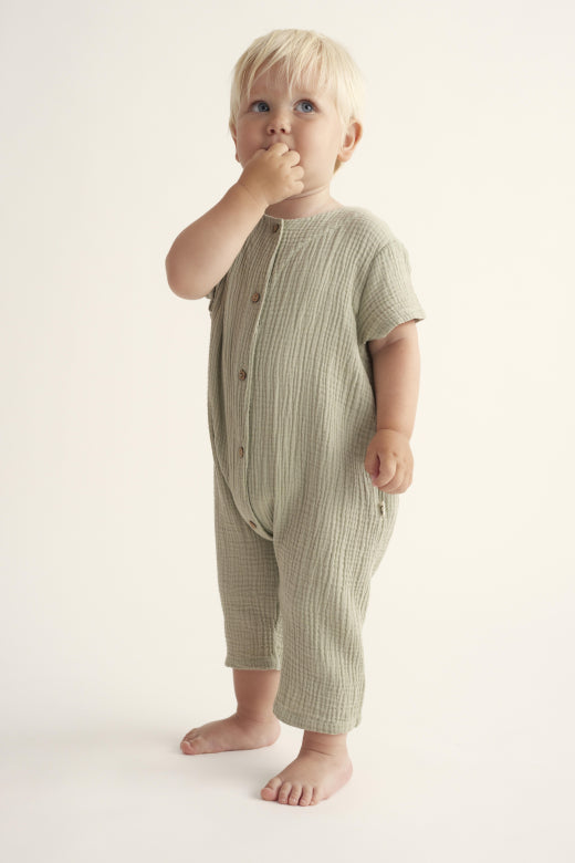 Unisex Strampler 'Luca' von Cozmo, getragen von einem Baby. Stilvolles und funktionales Design aus leichtem Musselin-Stoff.