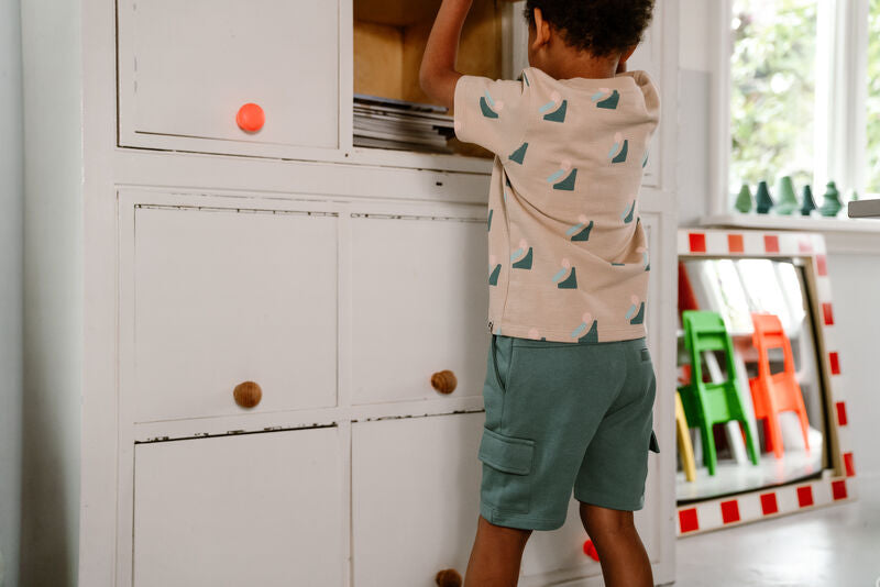 Kind zeigt die Cargo Shorts in Ocean Green von Daily Seven in einer spielerischen Indoor-Szene.
